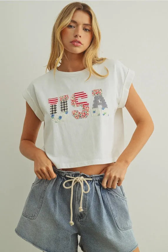 White cropped t-shirt featuring usa floral patchwork lettering in red white and blue patterns on the front