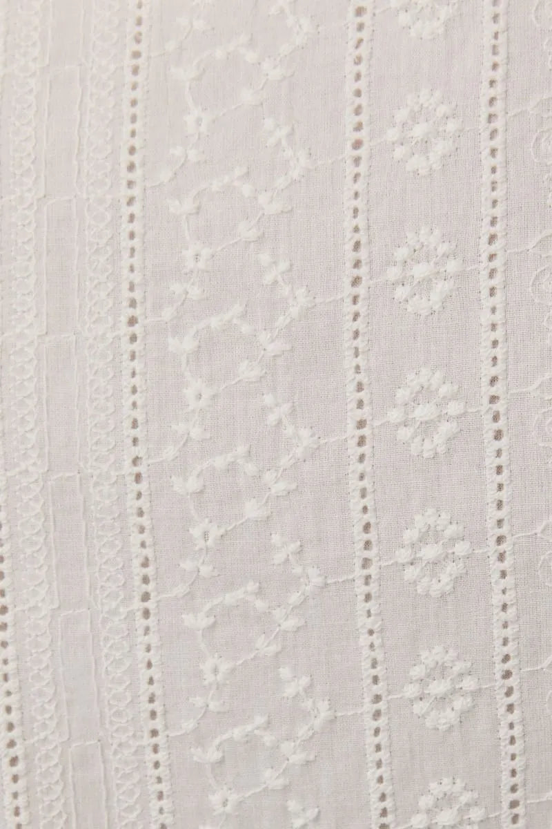 White embroidered lace fabric with delicate floral and vine patterns on a sleeveless eyelet mini dress