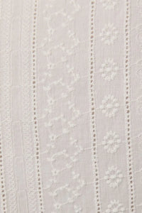 White embroidered lace fabric with delicate floral and vine patterns on a sleeveless eyelet mini dress