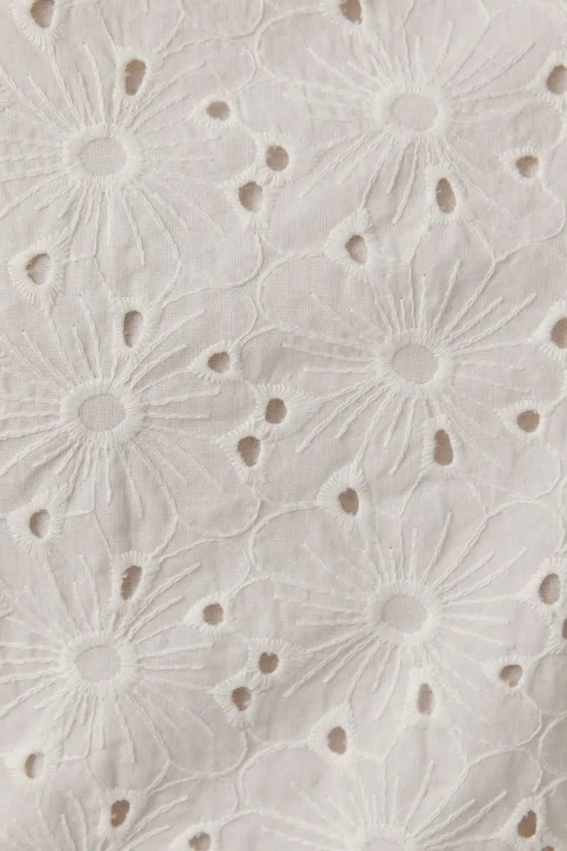 White eyelet sleeveless high neck top with delicate floral pattern and high neck bow detail