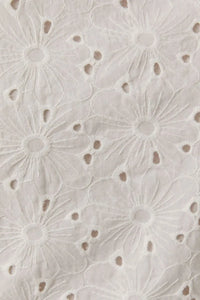 White eyelet sleeveless high neck top with delicate floral pattern and high neck bow detail