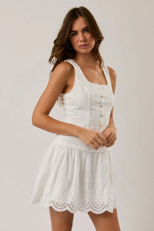 Sleeveless eyelet mini dress in white with button front and scalloped hem crafted from eyelet lace fabric