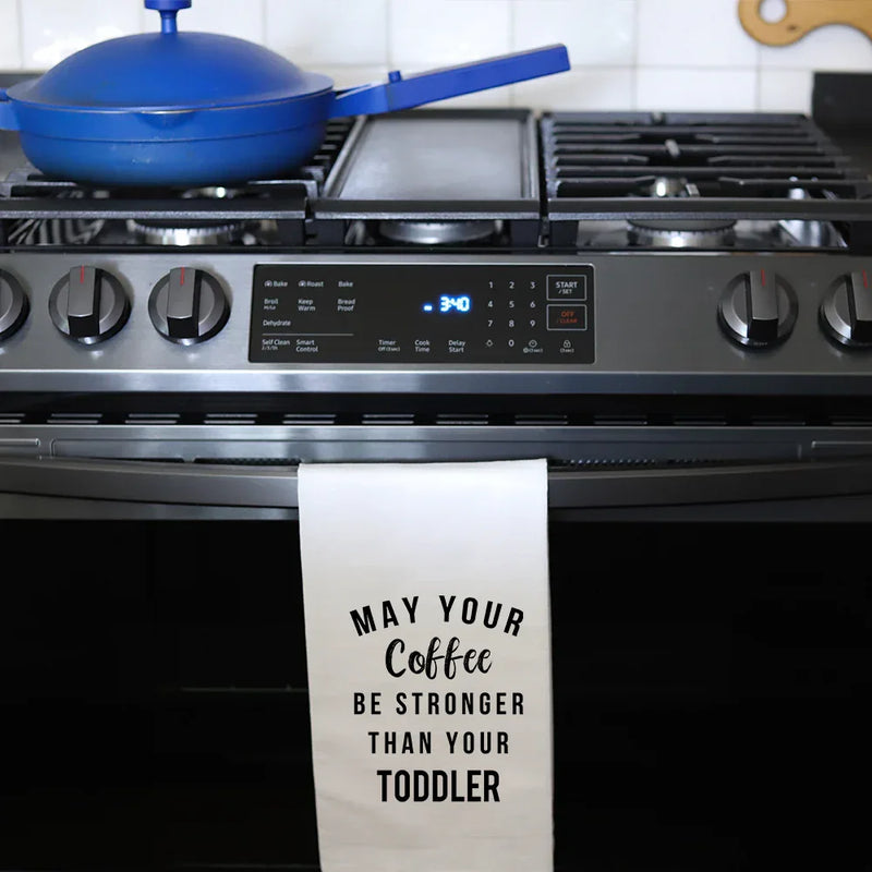 White kitchen tea towel with black text May your coffee be stronger than your toddler on oven handle
