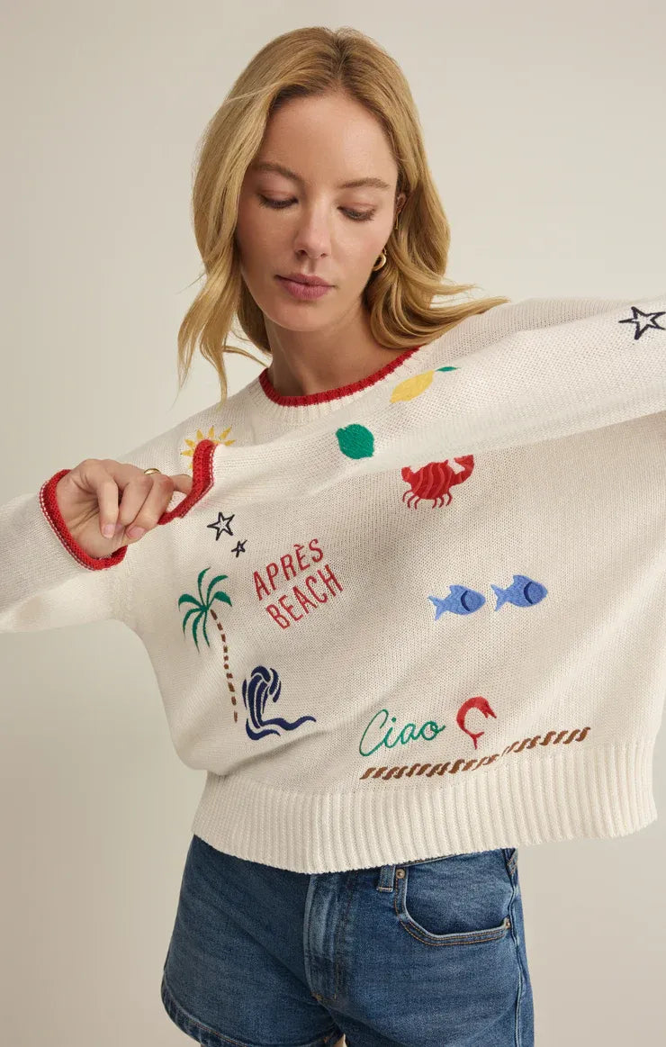 A white knitted sienna sweater with colorful embroidered beach motifs and red trim from the day sienna collection