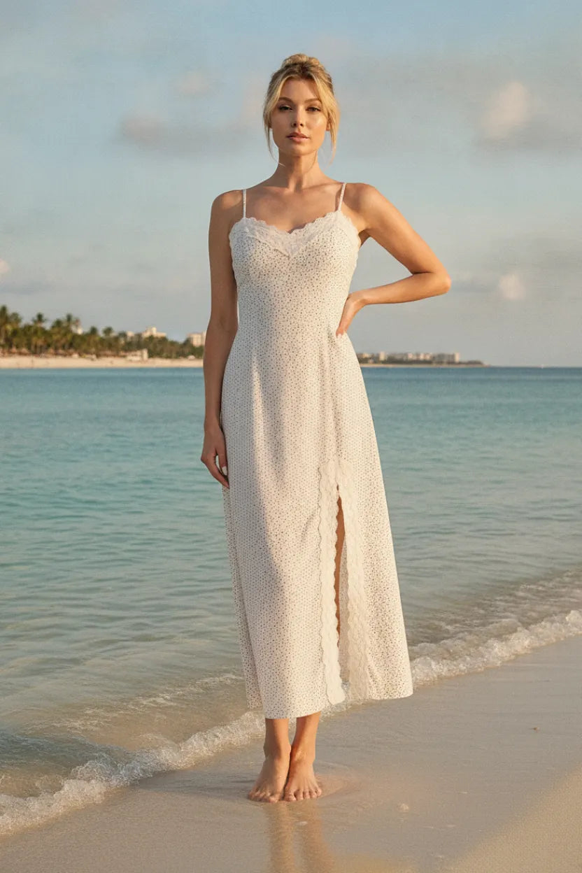 A flowing white lace maxi dress with delicate spaghetti straps, high slit, and scalloped lace trim details