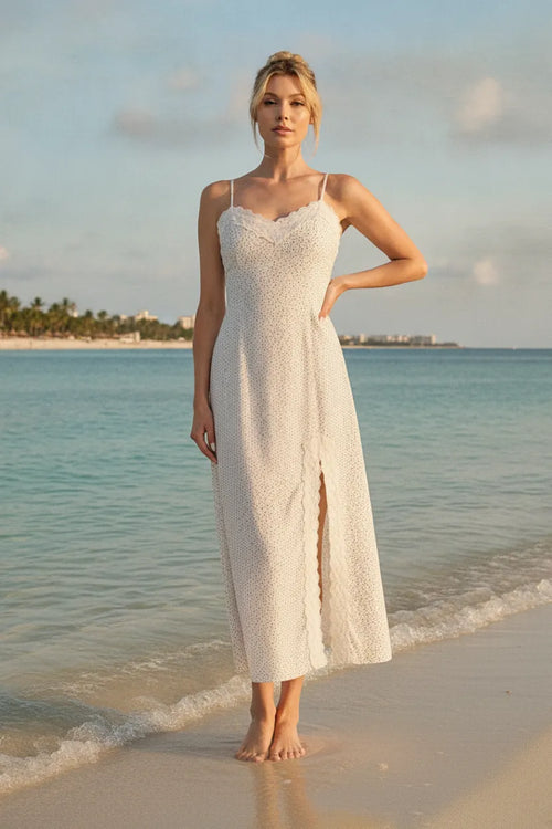 A flowing white lace maxi dress with delicate spaghetti straps, high slit, and scalloped lace trim details