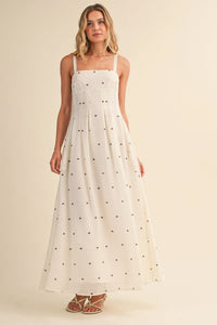 A flowing white maxi dress with delicate black polka dot print, thin spaghetti straps, and pin tuck detailing