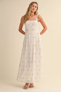 A flowing white polka dot pin tuck maxi dress with delicate black dots and thin spaghetti straps