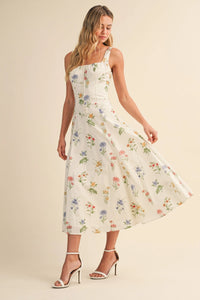 A flowing white midi dress with floral tie back lace up detail featuring delicate pastel flowers and spaghetti straps