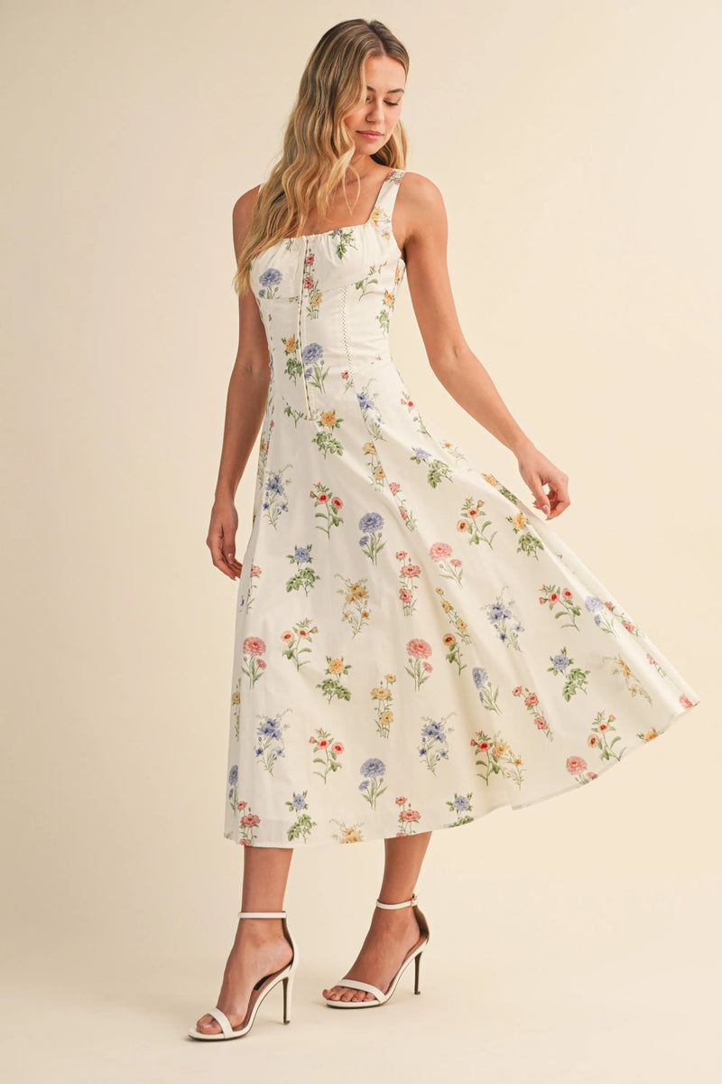 A flowing white midi dress with floral tie back lace up detail featuring delicate pastel flowers and spaghetti straps