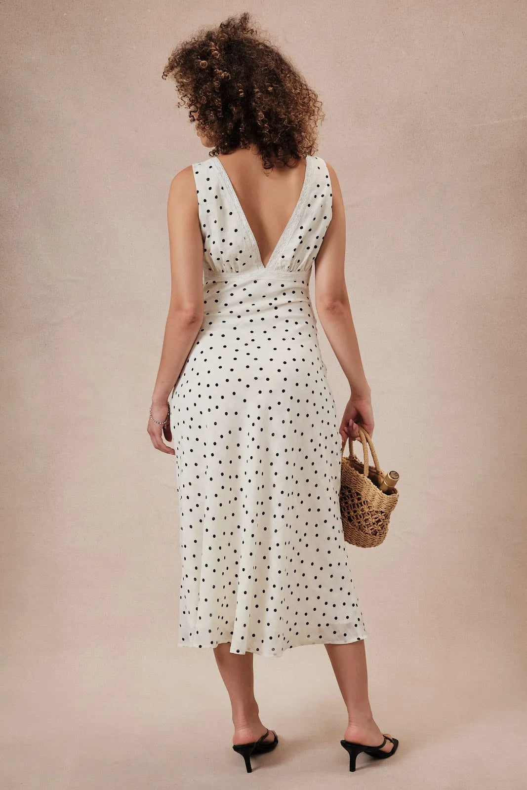 A flowing white sleeveless midi dress with black polka dots and lace detail featuring a deep v-back view
