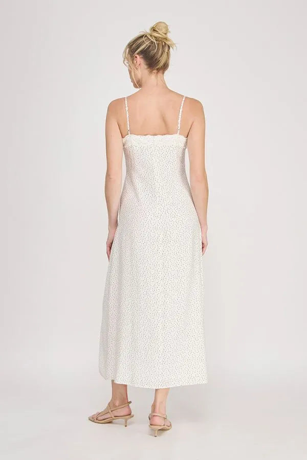 A flowing white midi slip dress with delicate spaghetti straps, subtle floral pattern, scalloped lace trim, and slit