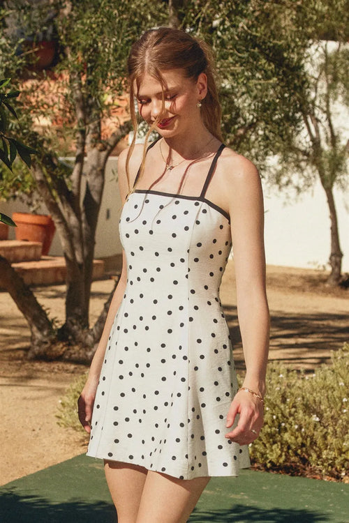 A white polka dot mini dress with contrast bind and thin black straps showcasing the back side
