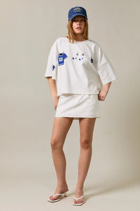 White oversized short sleeve americana top with blue jersey and cat face graphic paired with white mini skirt