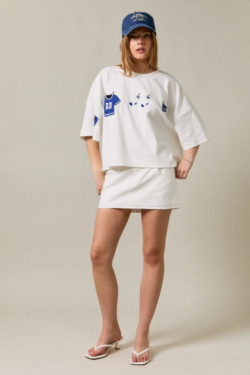 White oversized short sleeve americana top with blue jersey and cat face graphic paired with white mini skirt