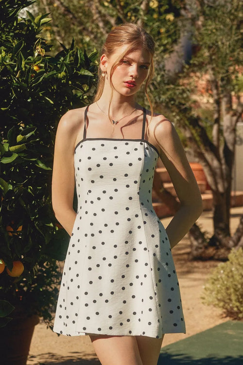 A white polka dot mini dress with black contrast bind thin straps and a flared skirt perfect for summer wear