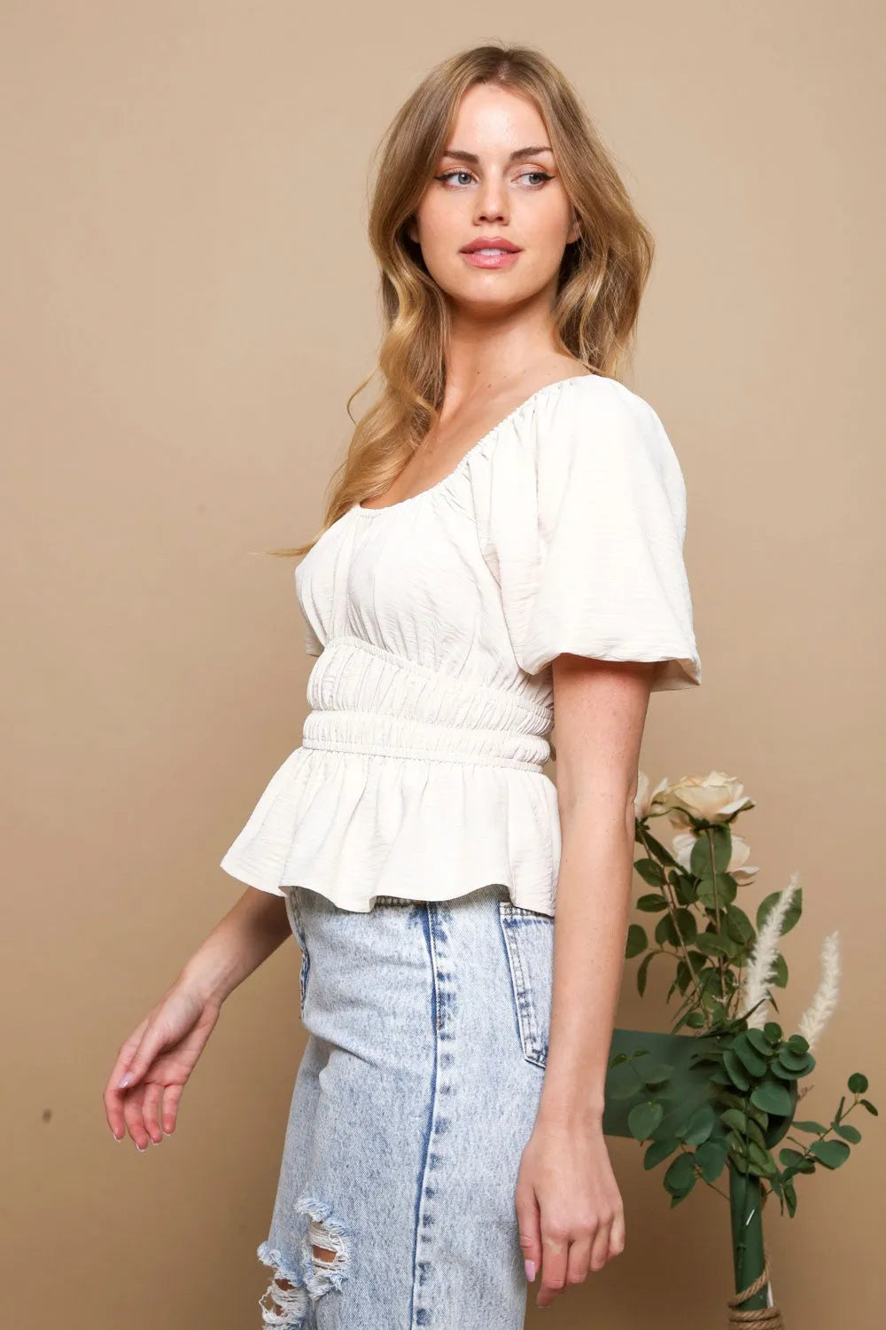 White top with short puff sleeves, ruched waist, smocked detail, and peplum hem in lightweight fabric