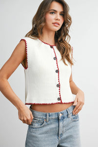 White ribbed sleeveless cardigan with red scalloped trim and black buttons