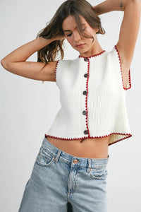 White ribbed knit sleeveless cardigan with red scalloped trim and black buttons