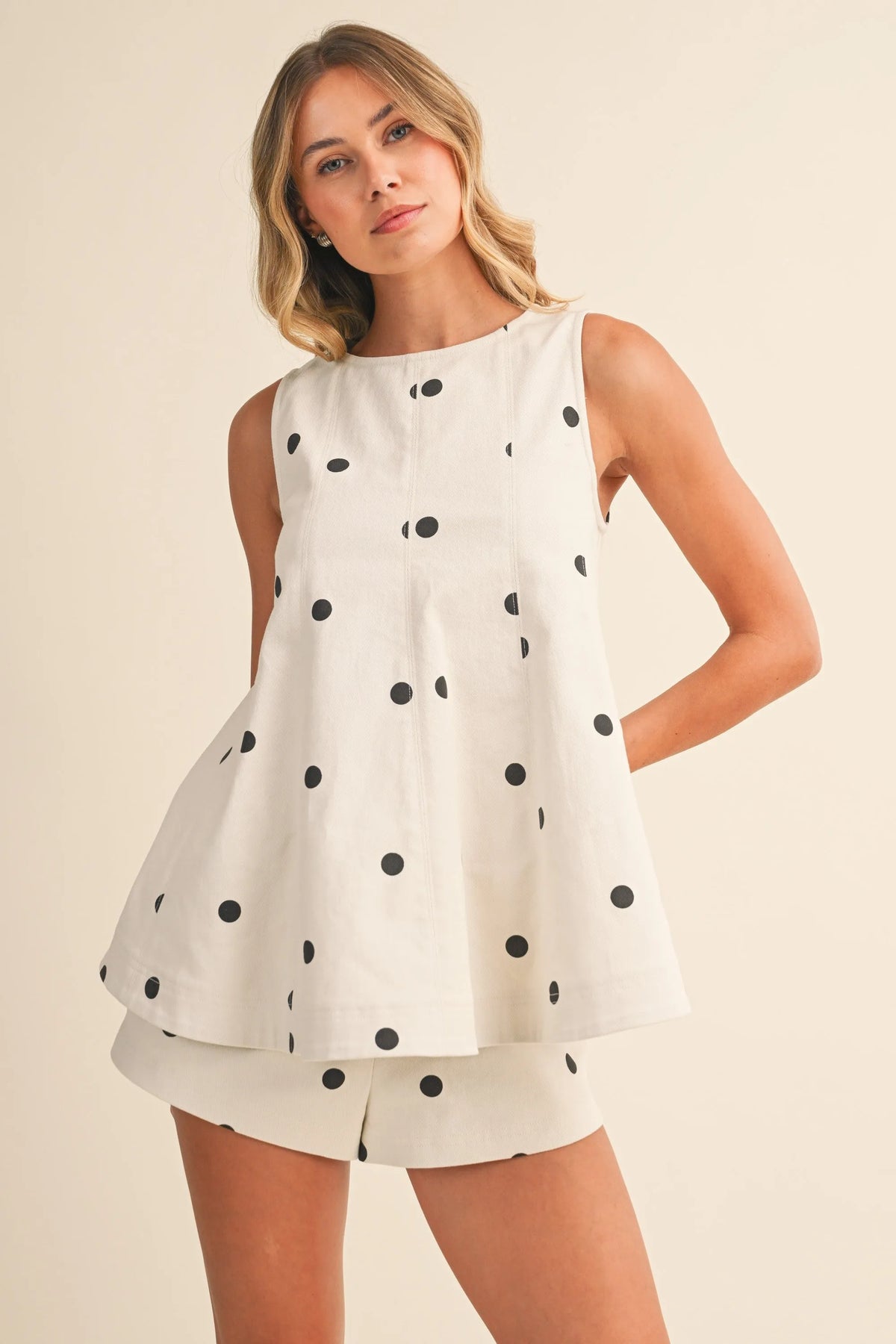 A white polka dot denim longline top with black dots and a flared tiered hem in a sleeveless design