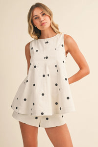 A white polka dot denim longline top with black dots and a flared tiered hem in a sleeveless design