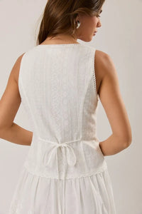 White sleeveless eyelet mini dress with intricate embroidery and tied waistband for elegant summer wear
