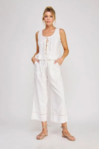 White sleeveless top with lace-up front and embroidery paired with white linen blend crop pants with lace detail