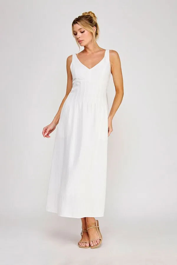 A flowing white sleeveless maxi dress with a v-neckline and pleated bodice maxi detail at the waist