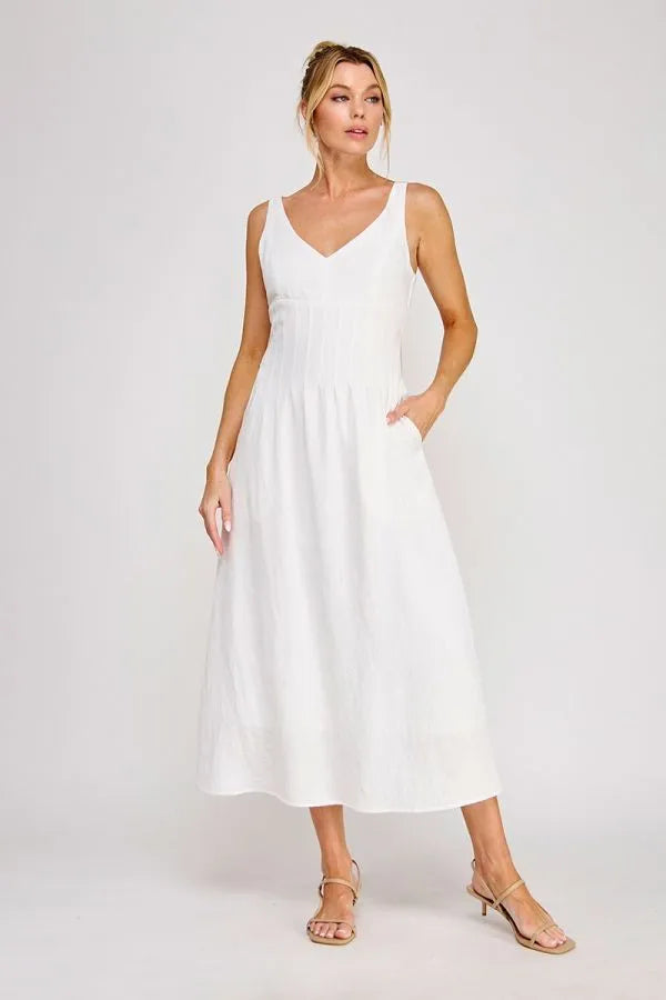 A flowing white sleeveless maxi dress with a v-neckline and pleated bodice detailing at the waist