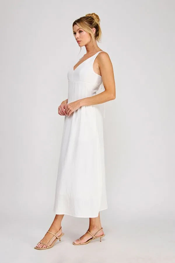 A flowing white sleeveless maxi dress with a v-neckline and pleated bodice detailing at the waist