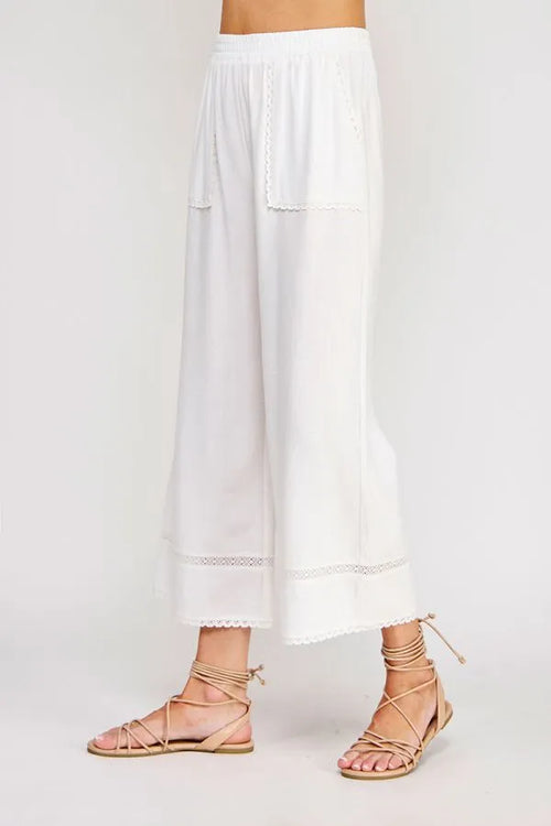 White linen blend crop pants with lace trim, soft cotton fabric, and subtle embroidered pockets in wide-leg style