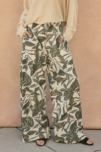 Cream base swaying palms wide leg pants featuring an olive green tropical leaf pattern and wide leg trousers design