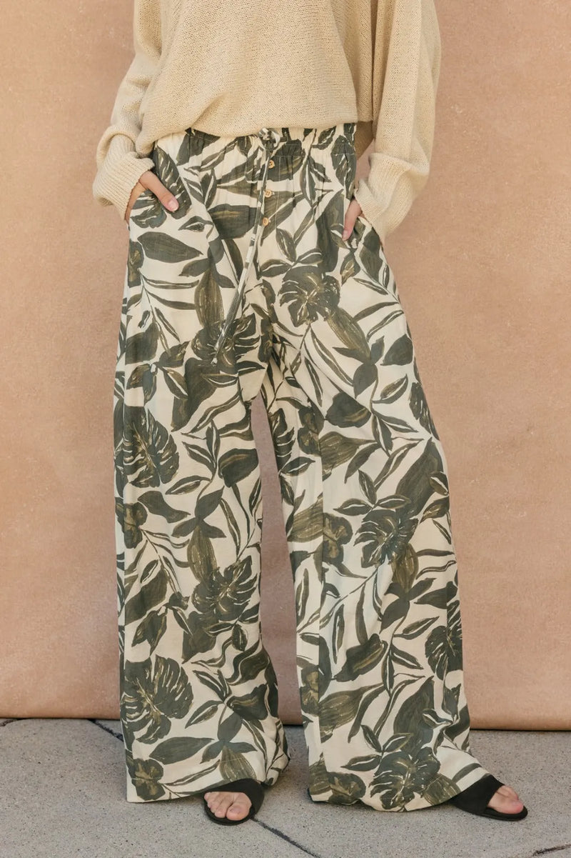 Cream base swaying palms wide leg pants featuring an olive green tropical leaf pattern and wide leg trousers design