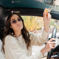 A woman holds a clear glass bottle car diffuser with a golden interior hanging air freshener for luxury scent