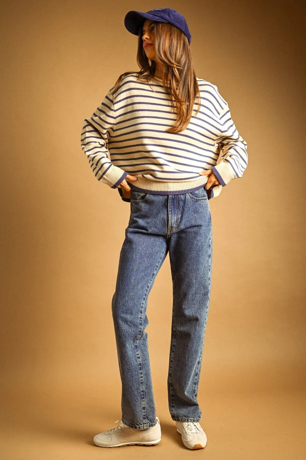 Woman wearing a navy and cream striped long sleeve sweater with ribbed cuffs paired with medium-wash blue jeans