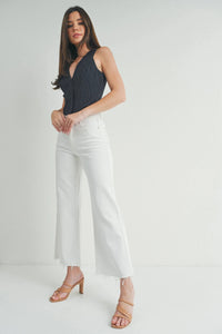 Woman wearing light wash slim wide leg jeans with frayed hems and a ribbed tank top