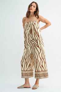 A woman wears a beige and brown border print jumpsuit with wide legs and geometric patterned cuffs