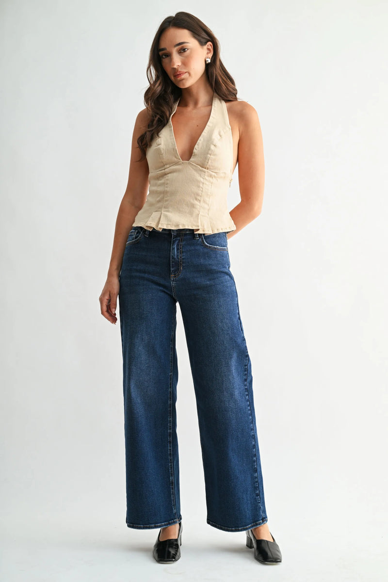 A woman wearing high rise vintage straight dark blue wide-leg denim jeans paired with a beige halter-neck corset top