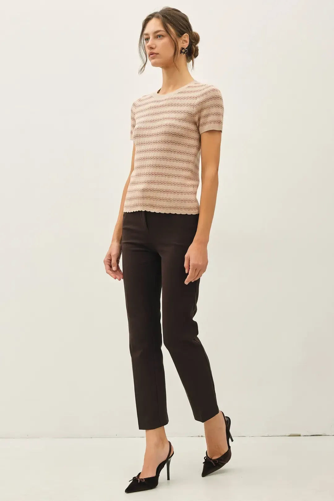 A woman wears a beige and brown scallop edge short sleeve sweater top paired with black cropped trousers