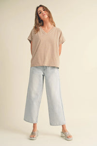 A woman wears a beige and white striped pattern short v-neck top with light-wash wide-leg jeans