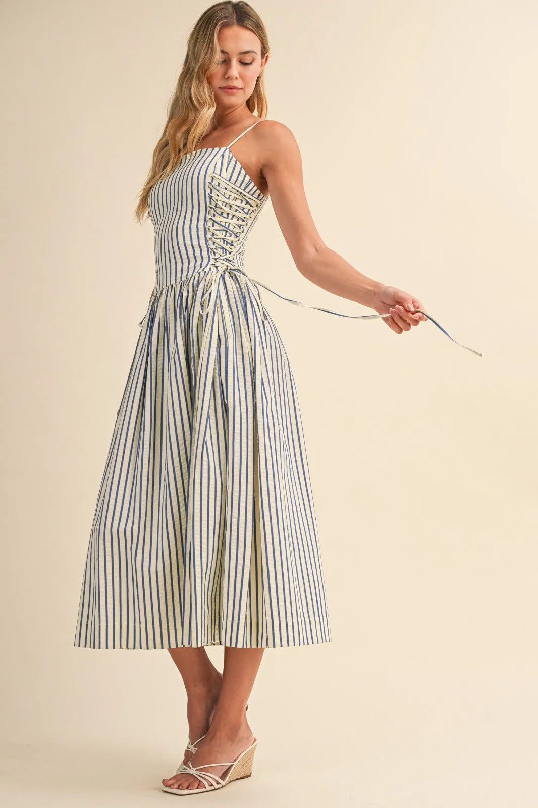 A woman wearing a blue and white striped midi dress with side tie detail and corset-style front lacing