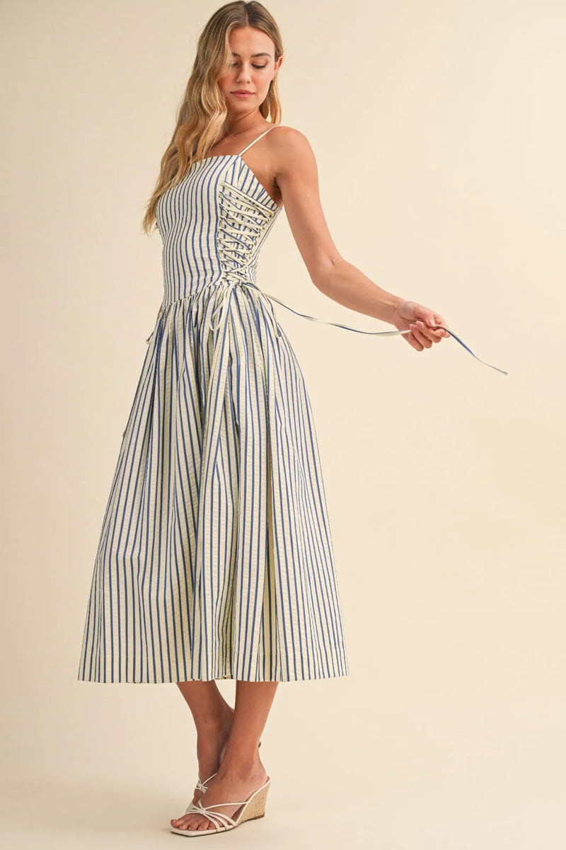 A woman wearing a blue and white striped midi dress with side tie detail and corset-style front lacing