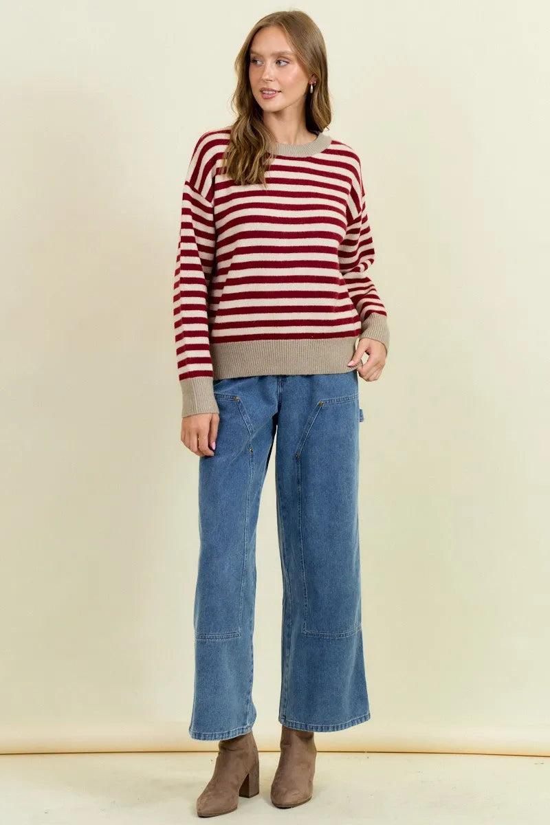 A woman wears a cozy round neck stripe color block sweater with bold red and white stripes and ribbed beige cuffs