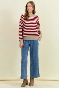 A woman wears a cozy round neck stripe color block sweater with bold red and white stripes and ribbed beige cuffs