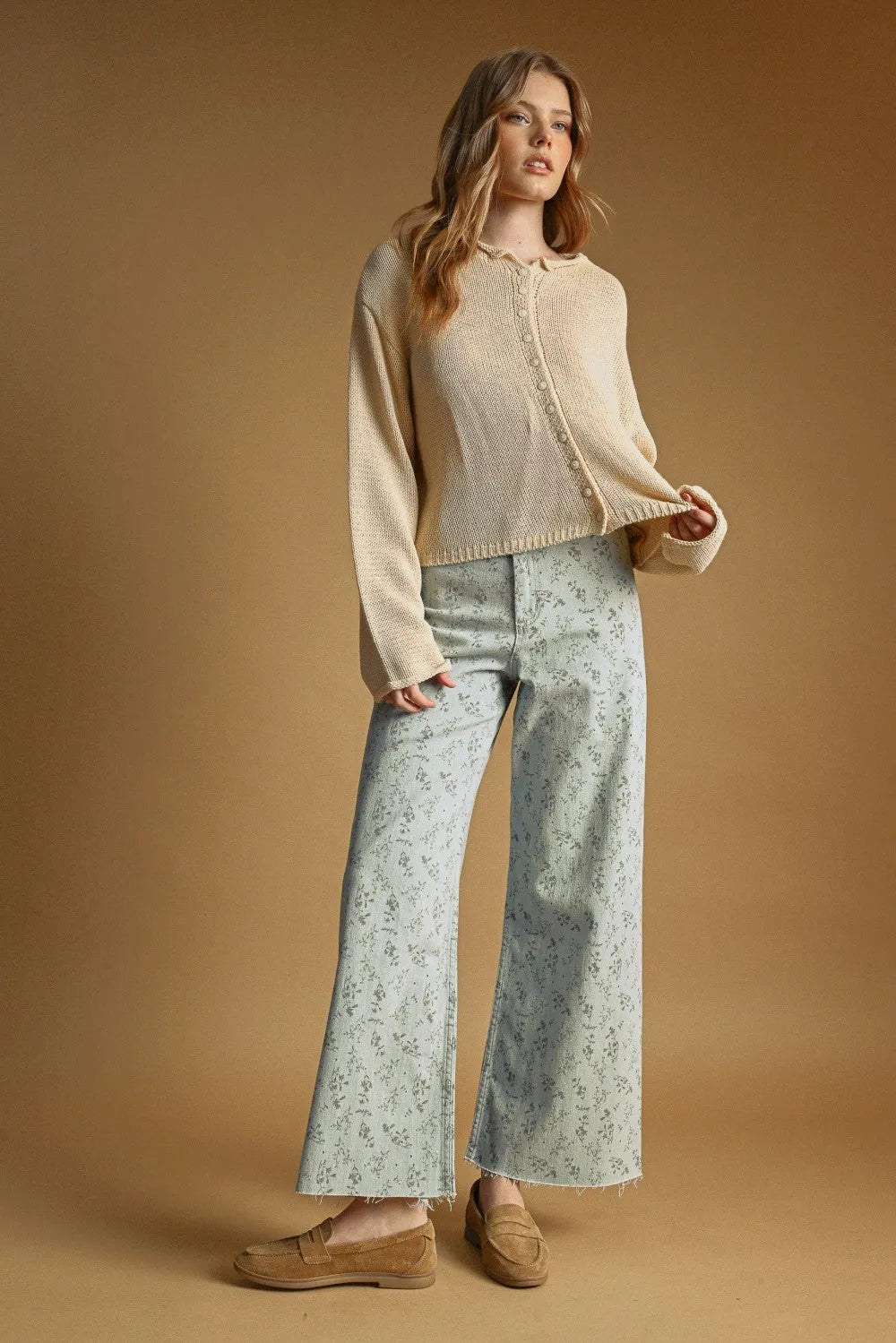 A woman wears a cream-colored easy knitted cardigan with button front and ribbed cuffs paired with floral pants