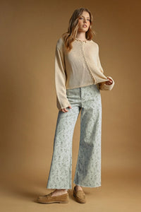 A woman wears a cream-colored easy knitted cardigan with button front and ribbed cuffs paired with floral pants