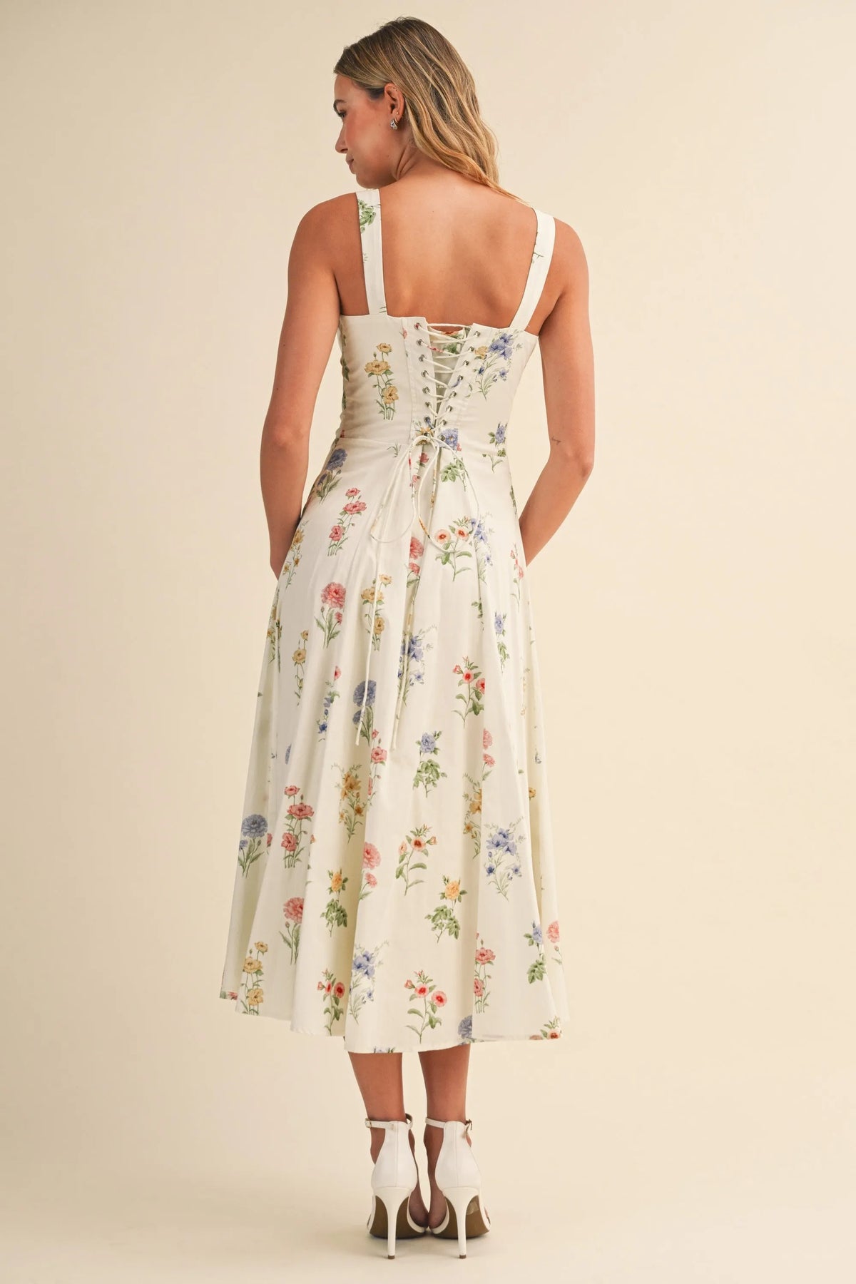 A woman wearing a cream floral tie back lace up midi dress with thin straps, perfect for women’s boho chic clothing