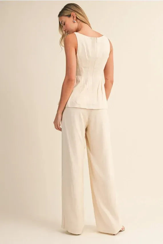 A woman wearing cream high rise wide leg pants with a fitted sleeveless peplum top shown from the back