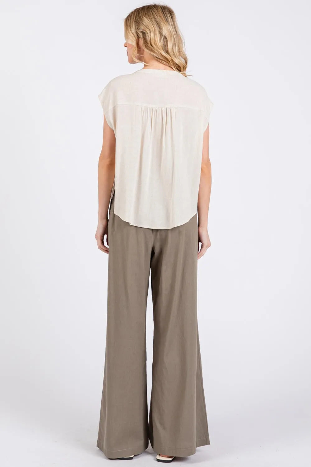 A woman wearing the back of a cream pintuck detailed button down shirt with short sleeves and wide-leg khaki trousers