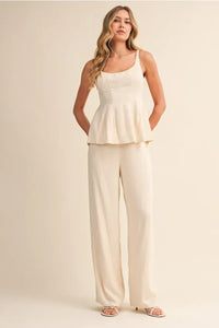 A woman wears a cream scoop neck zipper back blouse with sleeveless peplum and wide-leg trousers elegant outfit